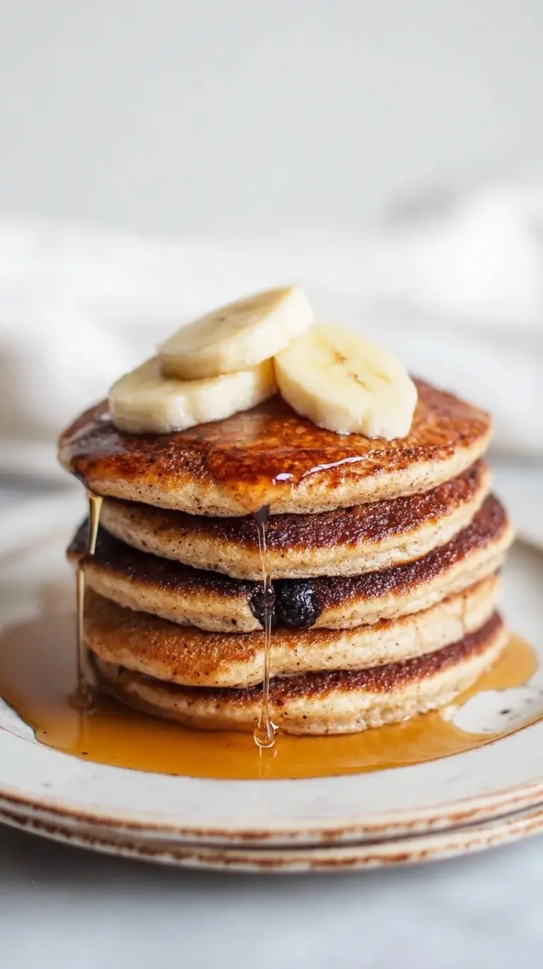 A stack of golden brown banana cottage cheese pancakes topped with fresh banana slices and syrup
