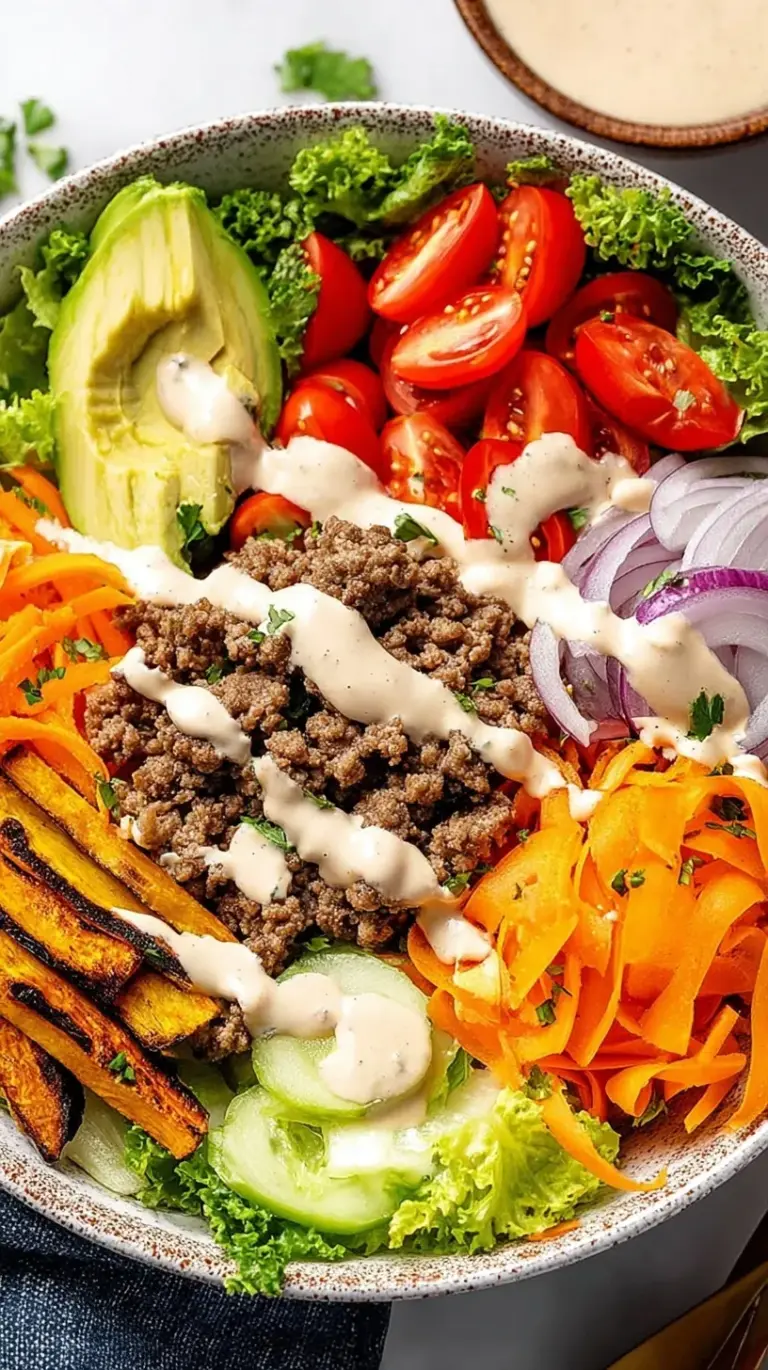 A vibrant bowl filled with seasoned ground beef, shredded lettuce, cheddar cheese, pickles, and a creamy orange sauce drizzle.