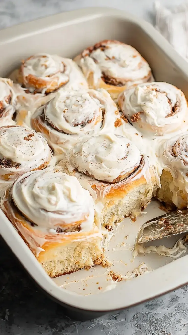 A tray of golden brown gluten-free cinnamon rolls topped with melting cream cheese frosting.