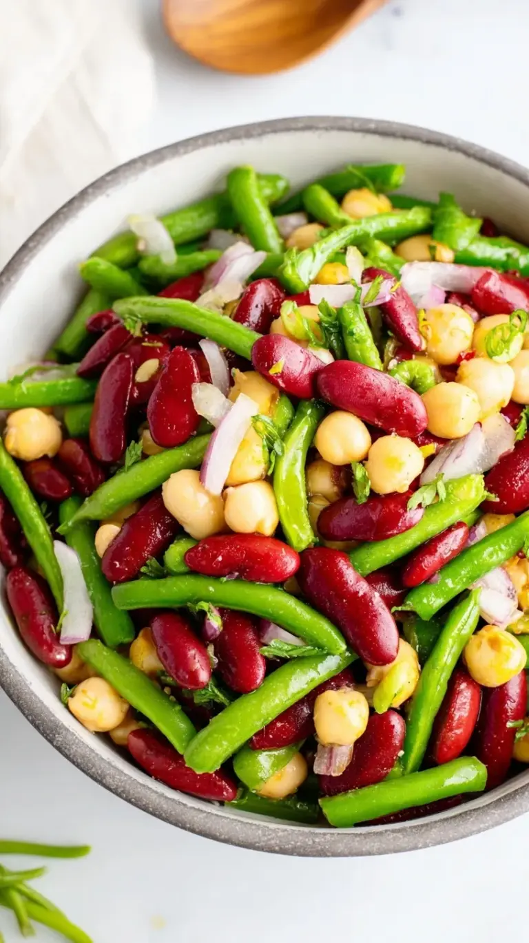 A colorful glass bowl filled with green beans, wax beans, kidney beans, and red onions in a zesty dressing.