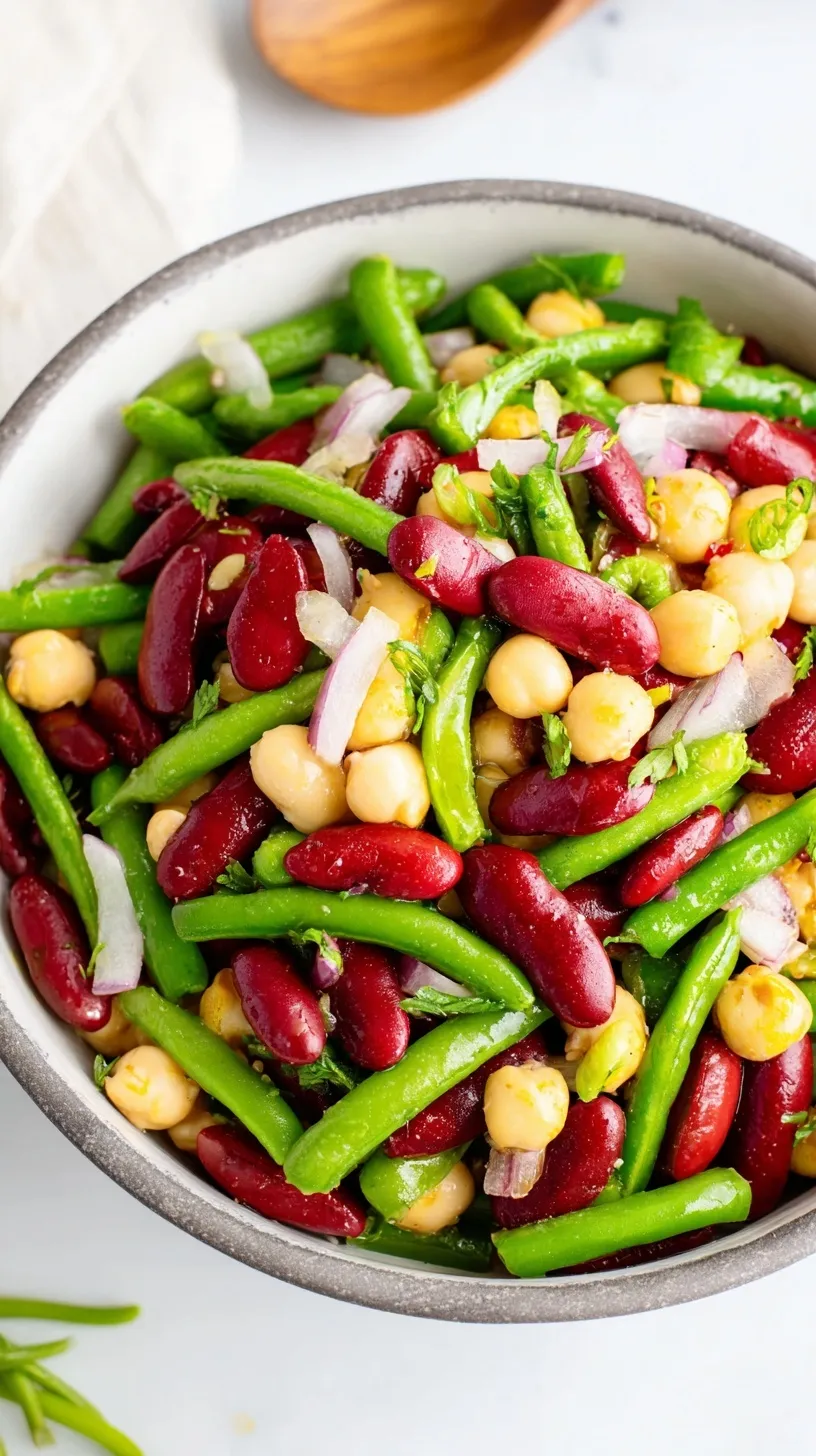 A colorful glass bowl filled with green beans, wax beans, kidney beans, and red onions in a zesty dressing.