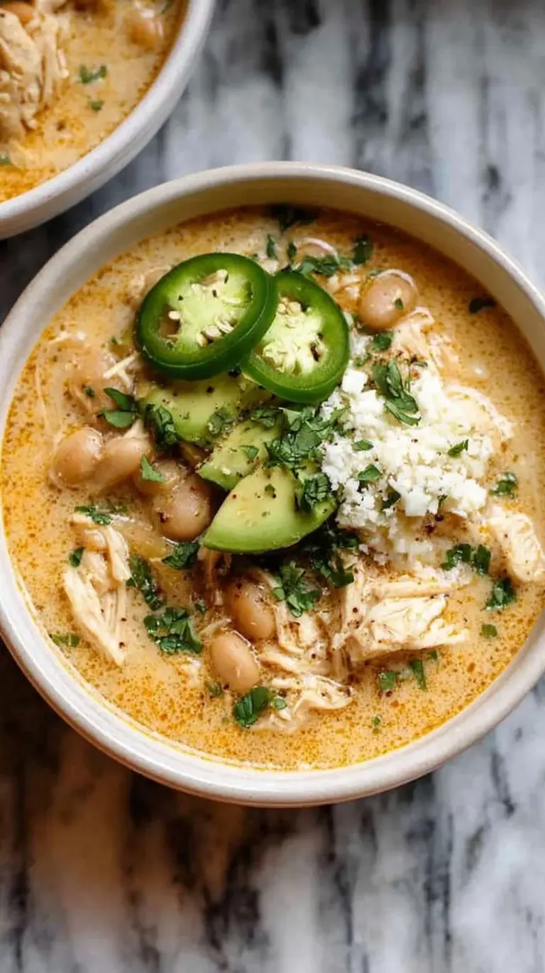 A white bowl filled with creamy chicken chili topped with cilantro and avocado