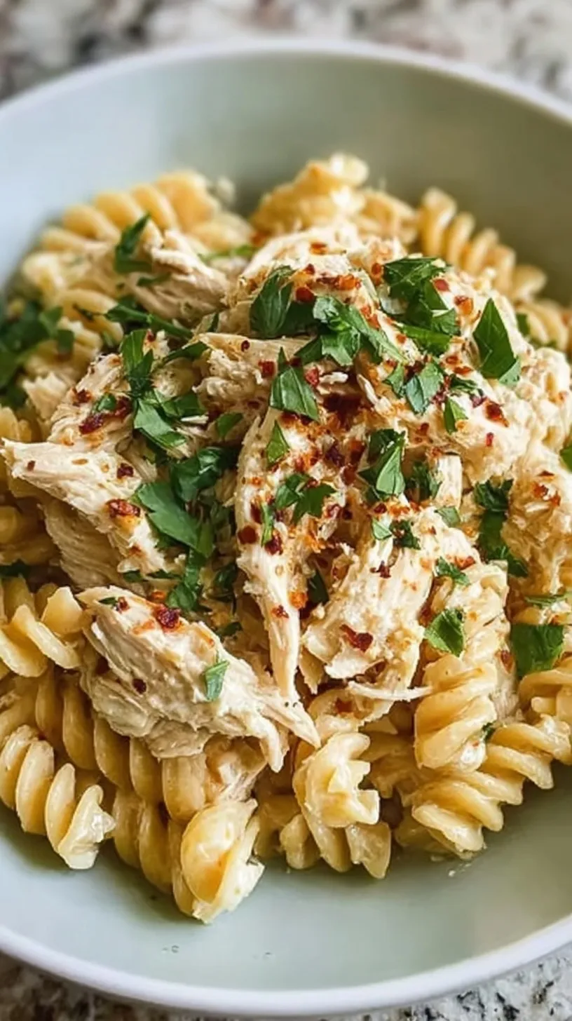 A white bowl filled with creamy garlic parmesan pasta and shredded chicken garnished with parsley.