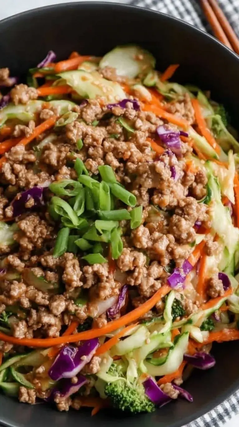 A vibrant bowl of ground turkey and shredded cabbage garnished with green onions and sriracha.