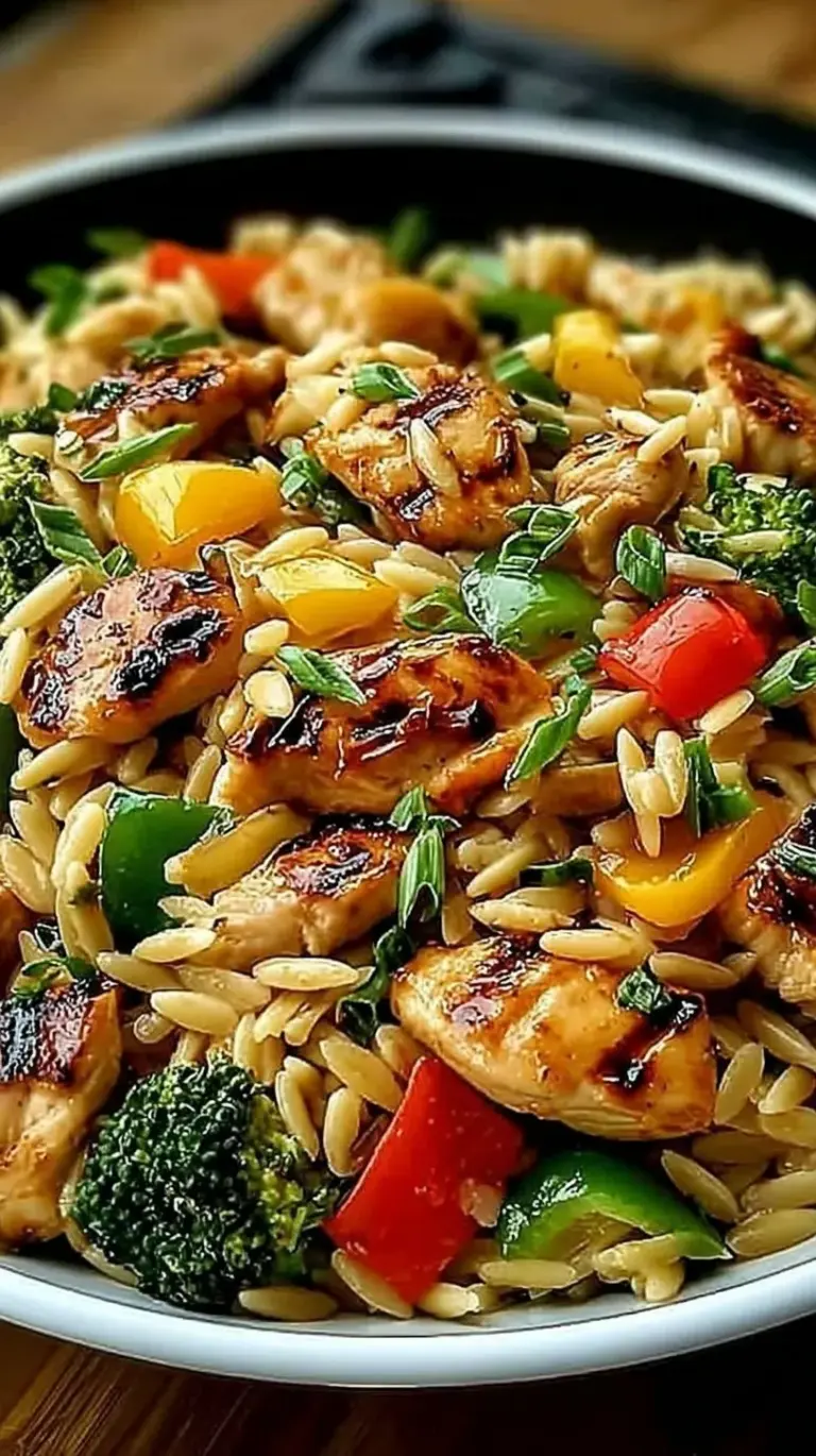 A colorful skillet of lemon chicken cubes, green zucchini, red peppers, and orzo pasta garnished with parsley.
