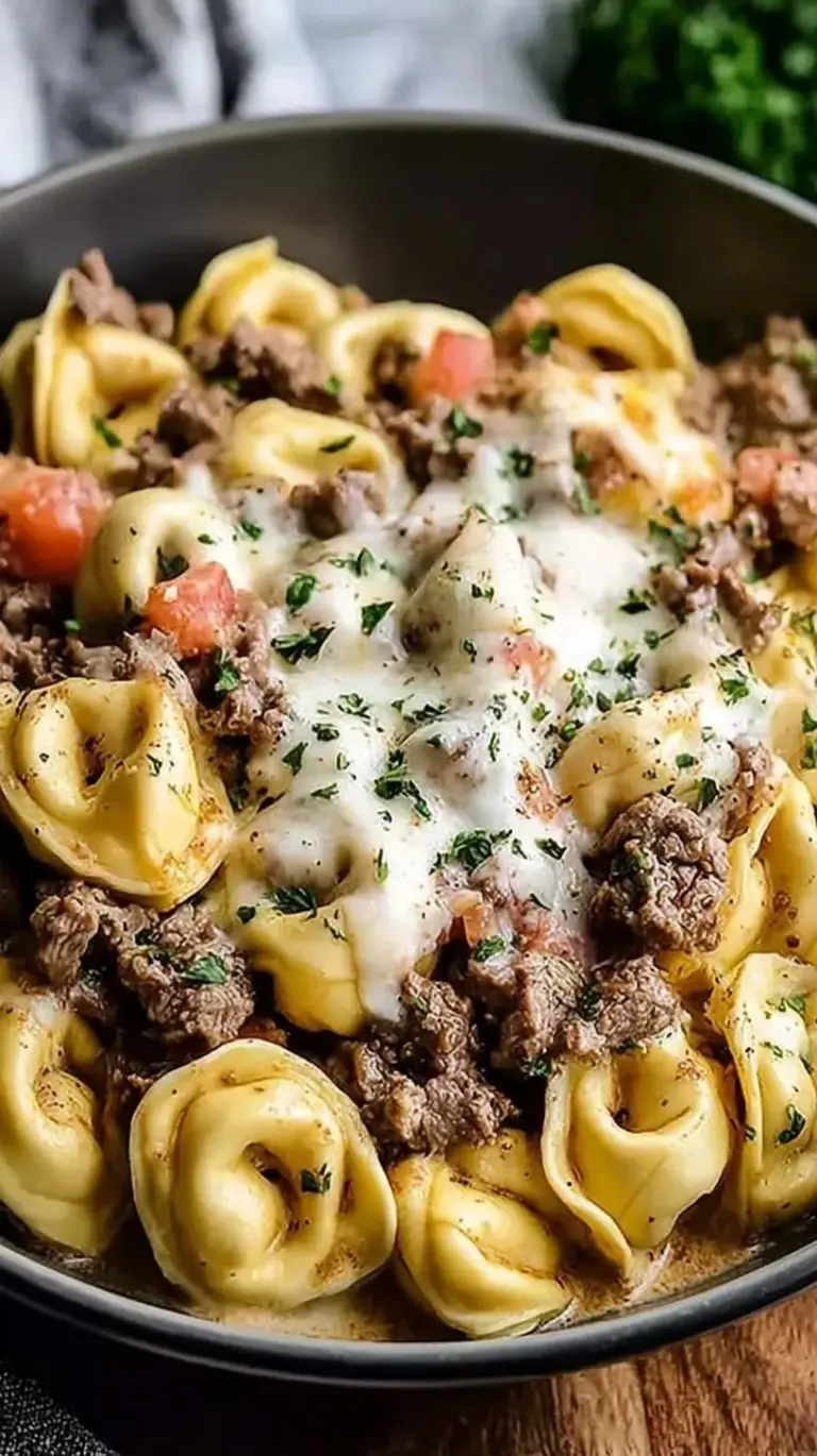 A skillet filled with Philly Cheesesteak Tortellini featuring sliced steak, green peppers, and creamy sauce.