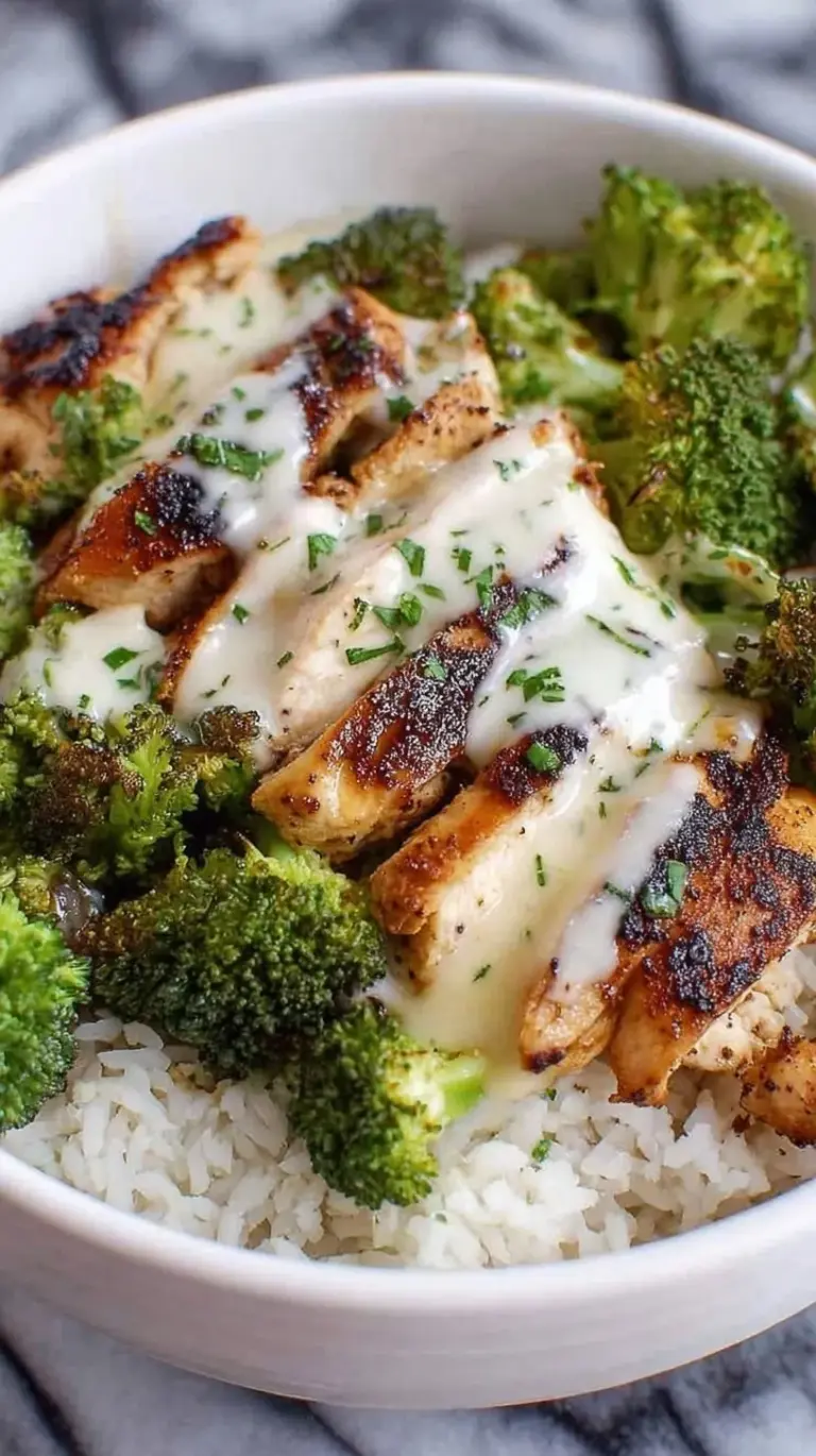 A white bowl filled with jasmine rice, seared chicken cubes, and green broccoli coated in a silky white garlic sauce.