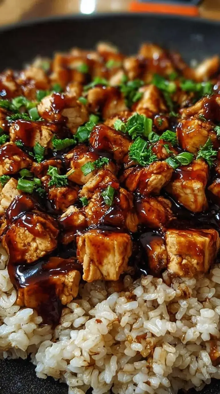 A skillet of golden BBQ chicken and fluffy rice garnished with green onions