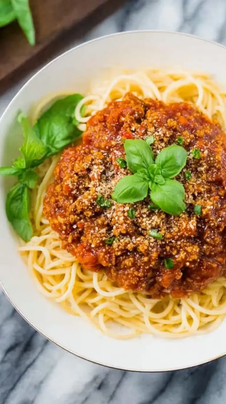 A bowl of pasta topped with thick, savory High Protein Tempeh Bolognese and fresh herbs.