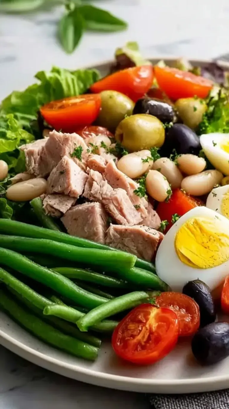 A colorful Nicoise-Style Tuna Salad with white beans, olives, and cherry tomatoes on a bed of greens.