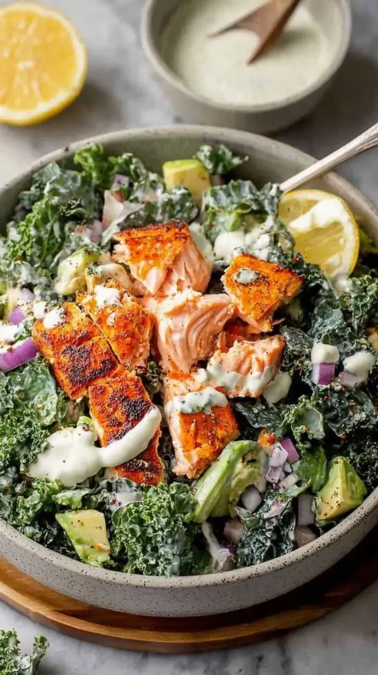 Pan-seared salmon fillet resting on a bed of dark green massaged kale with creamy dressing and croutons.