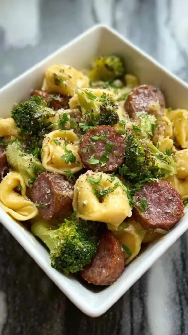 A colorful sheet pan filled with roasted cheese tortellini, sliced Italian sausage, zucchini, and cherry tomatoes topped with parmesan.
